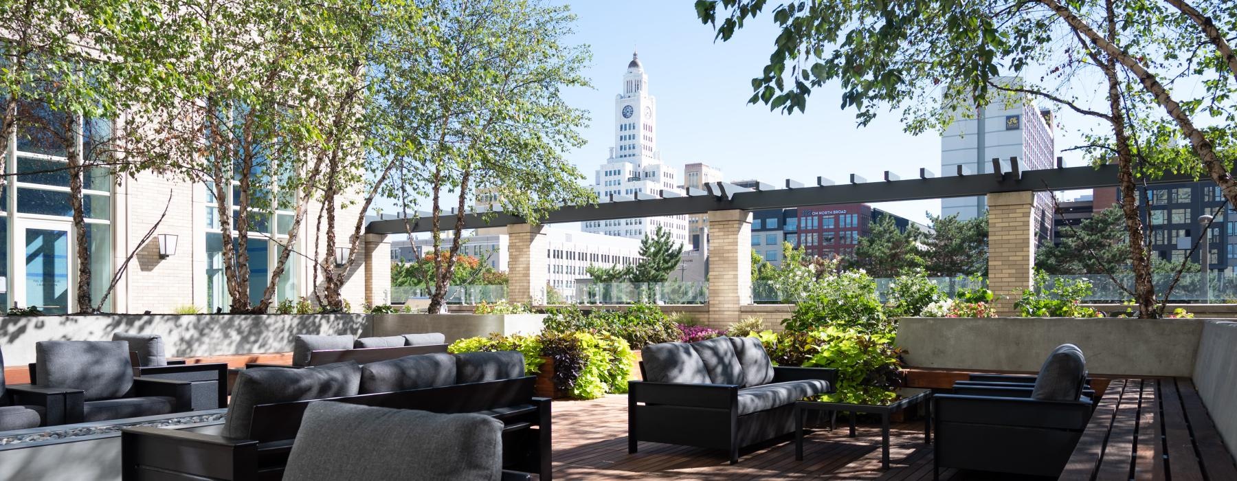 a patio with chairs and tables and trees with a city in the background